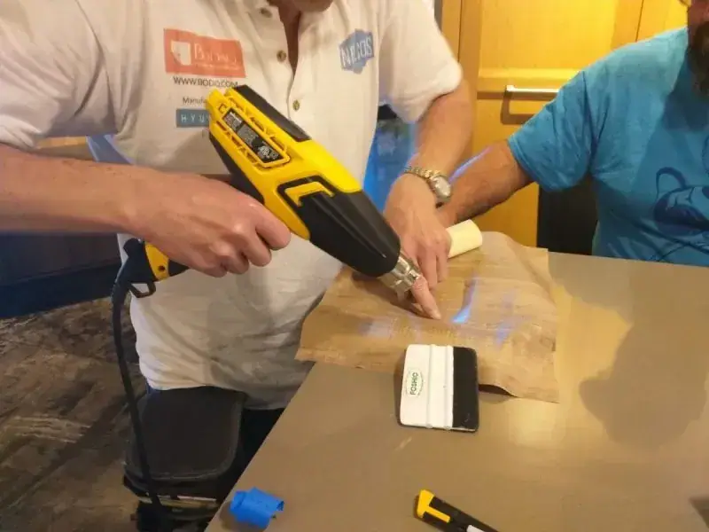 Hands heat-forming film around an edge with a heat gun and squeegee